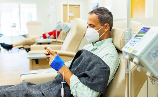 A man sits in a reclining chair on his phone while his infusion medication is administered
