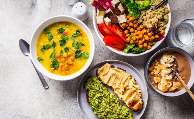 flat lay vegan food, chocolate smoothie bowl, Buddha bowl with tofu, chickpeas and quinoa, lentil soup and toast on gray background